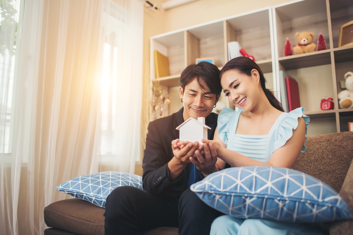 young-couple-holding-white-miniature-house-living-room (1)