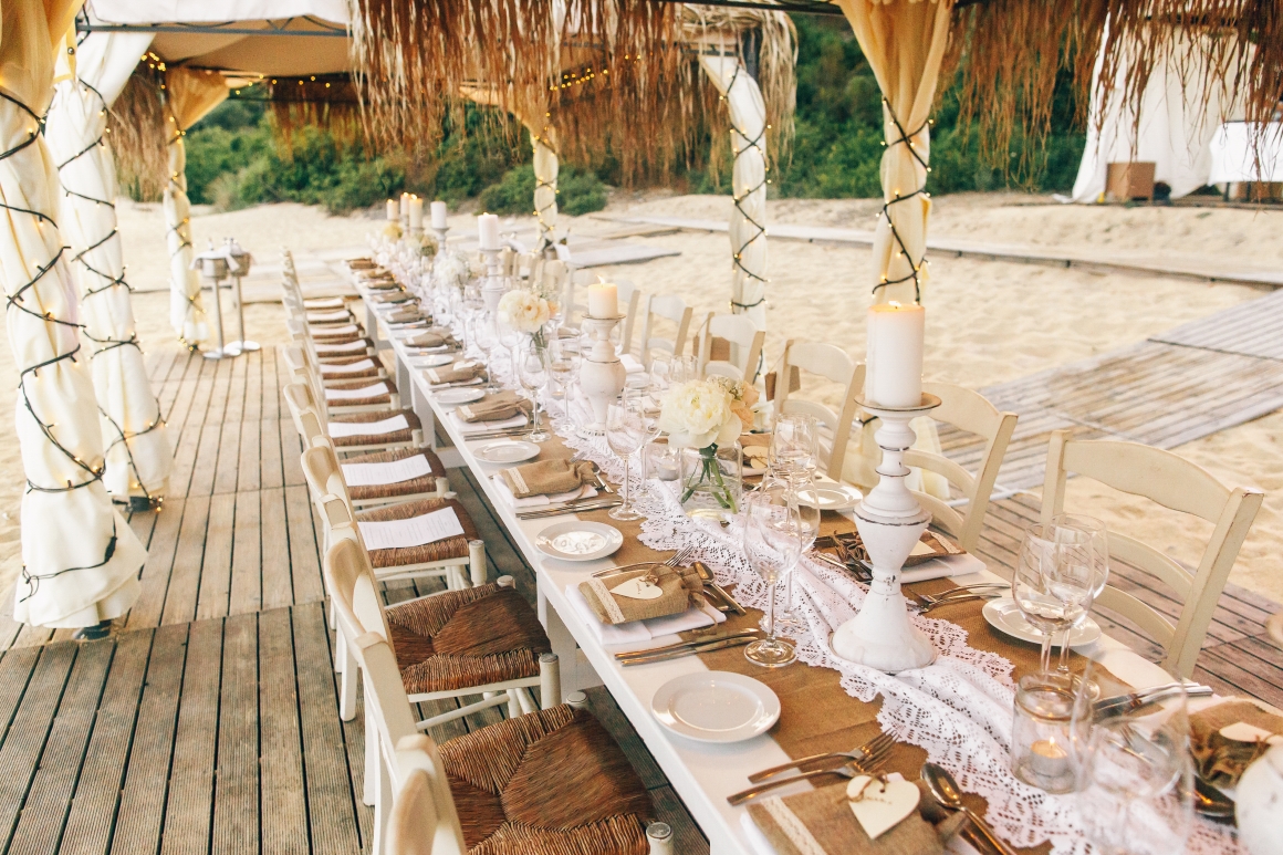 long-white-dinner-table-with-sparkling-glassware-candleholders-stands-beach long-white-dinner-table-with-sparkling-glassware-candleholders-stands-beach