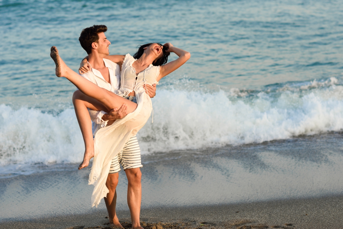 man-holding-woman-white-dress-beach