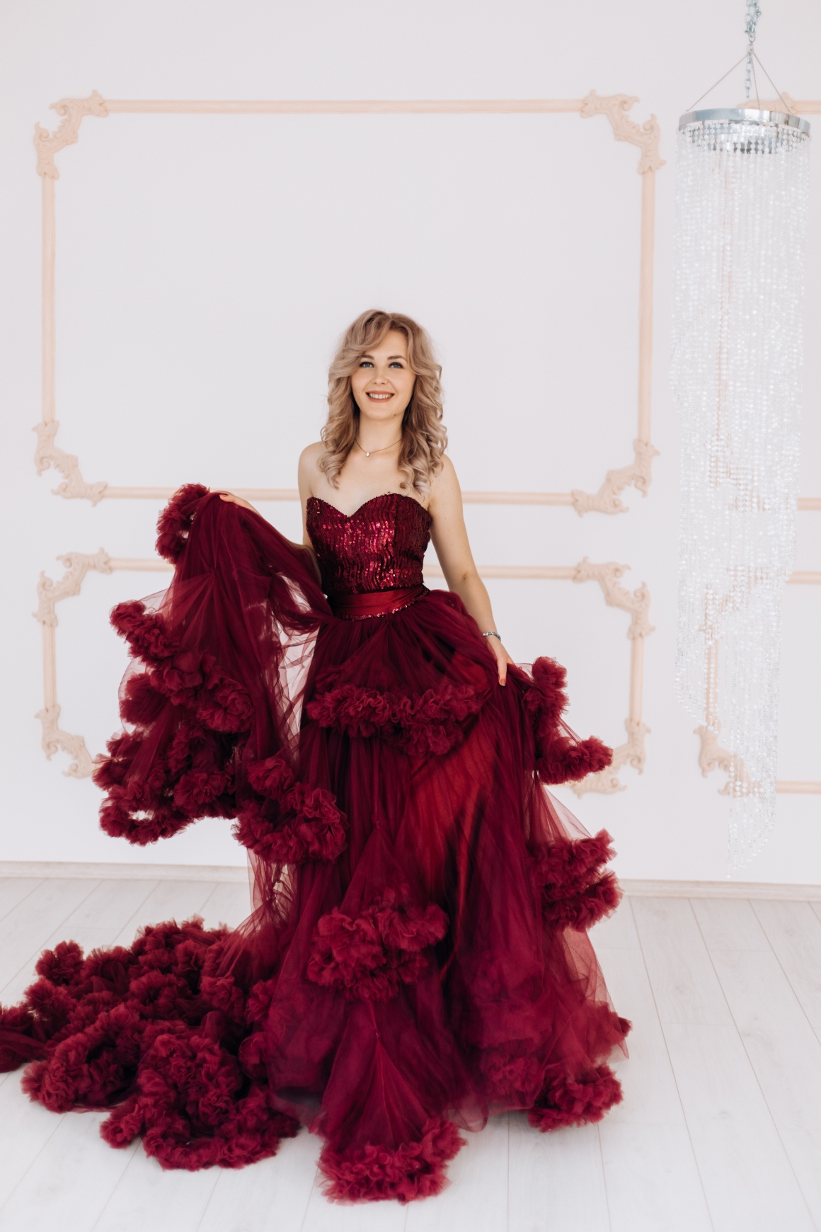 adorable-woman-red-burgundi-dress-poses-bright-luxury-room-with-large-chandelier